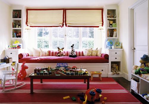a bright kid's space with a red daybed with pillows and toys and bookshelves built in on each side of the bed