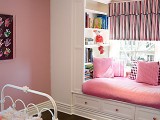 a cozy built-in window seat in pink, with lots of pillows and large built-in bookshelves on each side