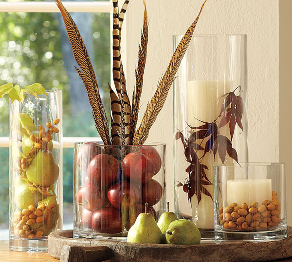 a cool fall centerpiece of glasses with faux fruit, feathers, dried leaves, nuts and acorns is very natural