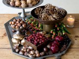 a multi-level fall display with nuts, pinecones, gilded pinecones, berries, candles and fruits