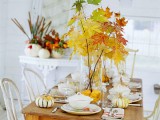a glass vase with pumpkins and branches with bold leaves is a cool and all-natural modern fall centerpiece