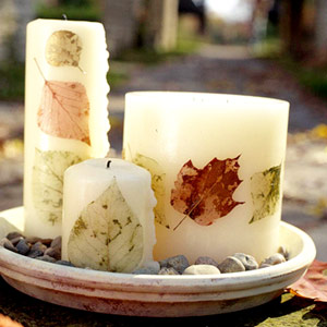 a wooden bowl with pebbles and pillar candles covered with colorful fall leaves is a cool fall centerpiece or decoration