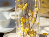 a tall glass vase with white pebbles and branches with berries is a cool fall decoration or centerpiece with a touch of color