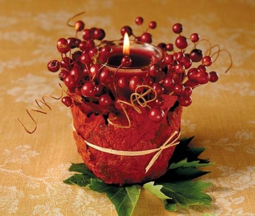 a cool fall wedding decoration of a glass candleholder with a red candle covered with faux leaves and berries