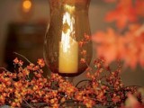 a candle lantern surrounded with berry branches and vines is a lovely fall centerpiece or decoration