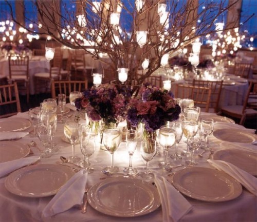 a refined fall wedding centerpiece of dark blooms, candles and branches with candleholders hanging on them
