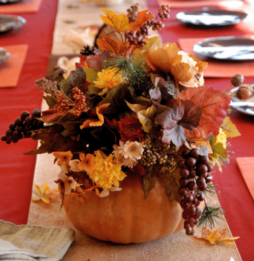 a natural fall wedding centerpiece of a pumpkin with bold leaves, blooms and berries cascading down looks lush and chic
