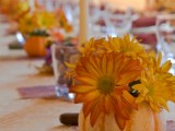 a pumpkin with bright blooms and candles in glasses for decorating the wedding reception table