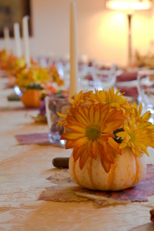 a pumpkin with bright blooms and candles in glasses for decorating the wedding reception table