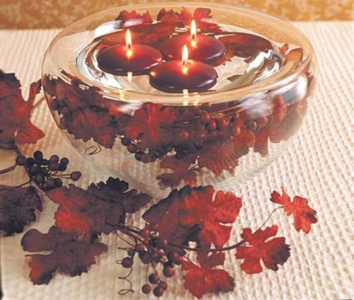 a glass bowl with bright leaves and berries and burgundy floating candles for decorating a wedding space