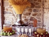 a fall wedding drink station with apple cider tanks placed on apples and a wheat bundle in a large vintage urn