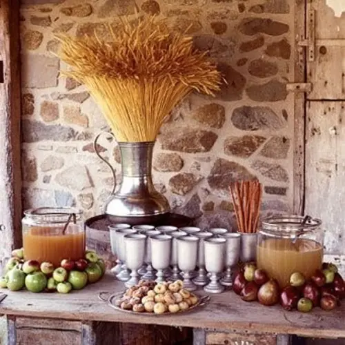 a fall wedding drink station with apple cider tanks placed on apples and a wheat bundle in a large vintage urn