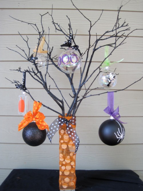 black branches placed in a vase wrapped with orange ribbons, with black and sheer glass ornaments and colorful ribbons
