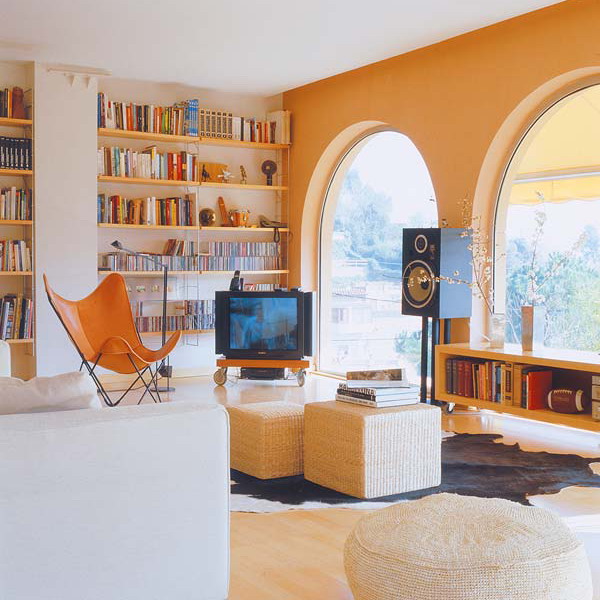 A mid century modern living room with open bookshelves attached to the wall and a floor book storage unit next tot he window