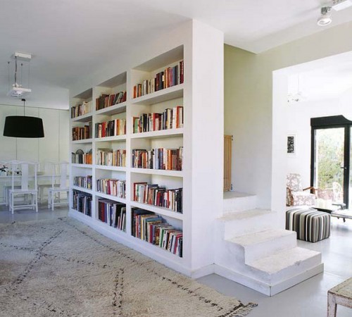 a built-in bookcase covers the whole wall and separates the staircase from the rest of the space