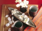 a beautiful zen arrangement with a bamboo mat, pebbles, cups, a bowl with blooms