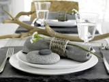 a natural coastal setting with a grey napkin with a wicker napkin ring, some pebbles and driftwood as a centerpiece