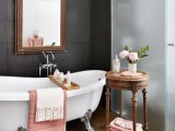an eclectic bathroom with a dark statement wall, a vintage tub, an ornate mirror and a frosted glass shower