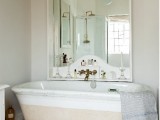 a retro coastal bathroom in neutrals, with a large tub, a statement mirror with a shelf and a large shell for storage