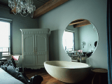 a vintage bedroom with a crystal chandelier, a large oval tub and a round mirror over it for an eclectic look