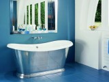 a modern blue bathroom wtith a white wall, a metal clad bathtub and a large mirror over the tub