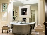 a refined vintage bathroom in neutrals, with a metal clad tub, upholstered ottomans and a mirror wall with an artwork