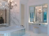 a luxurious bathroom in white marble, with a crystal chandelier, a mirror clad bathtub and a mirror over it for a statement