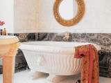 a quirky and refined bathroom done in marble and stone, with a bowl-like bathtub, an ornate mirror, a stone table
