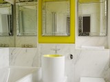a contemporary bathroom done with white marble, several mirrors, a bathtub and a round sink all done in white marble