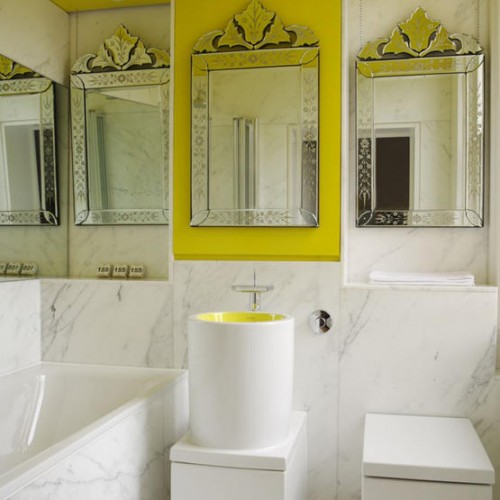 a contemporary bathroom done with white marble, several mirrors, a bathtub and a round sink all done in white marble