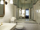 a retro bathroom with floral walls, white subway tiles, touches of gold and brass and a large arched mirror over the tub
