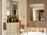 a refined bathroom with neutral furniture, a stone enclosed bathtub, pillar candles and a large ornate mirror over the tub
