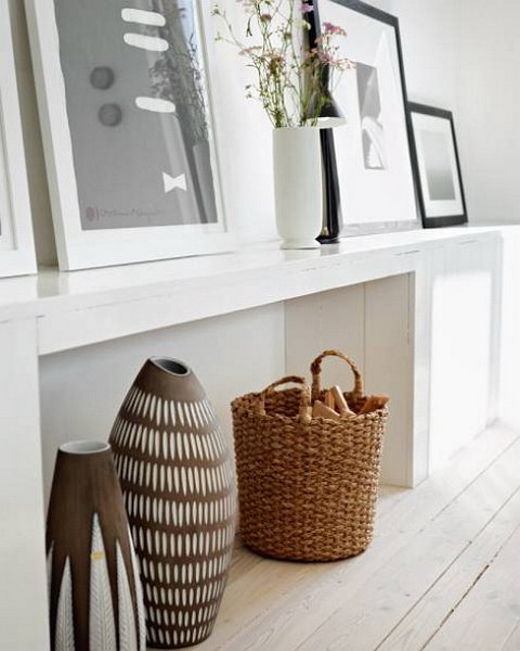 a white narrow console table and a basket for storage firewood is a decoration that adds coziness to the space