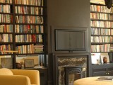 a stylish home library featuring built-in bookshelves, a fireplace and a TV that merges with the black wall and doesn’t look too much in your face