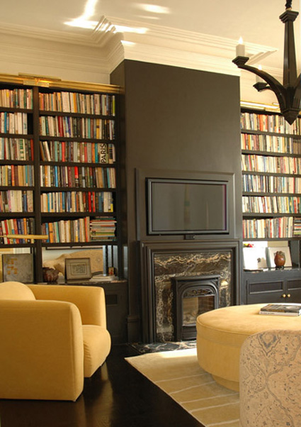 a stylish home library featuring built-in bookshelves, a fireplace and a TV that merges with the black wall and doesn't look too much in your face