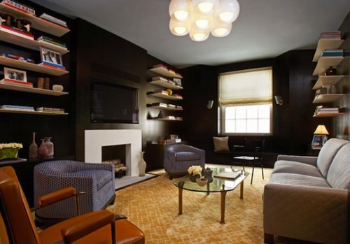 a mid-century modern living room with black walls, bookshelves, a fireplace, mismatching chairs and a sofa plus a TV over the fireplace that merges with the black wall