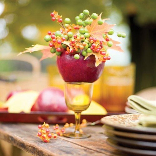 a red apple with fall leaves and berries placed on an amber glass is a cool fall decoration to try