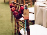 a red apple garland with ribbons and tags hung on a chair back is a cool decoration for a fall wedding or a party