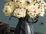 a beautiful and scary Halloween centerpiece of a black vase with white roses and spiders plus a black snake