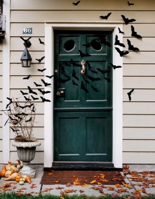outdoor Halloween decor with lots of paper bats attached to the walls and door, fall eaves and stacked pumpkins