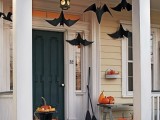 oversized paper bats hanging over the porch and stackes of pumpkins and brooms make the space look very Halloween-inspired