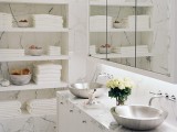 a refined bathroom clad with white marble and niches that are used for storage, a floating vanity and a large mirror