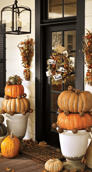 cozy traditional Thanksgiving porch decorating with stacked pumpkins in natural colors, fall leaves and cool bundles and a wreath with leaves, acorns and wheat