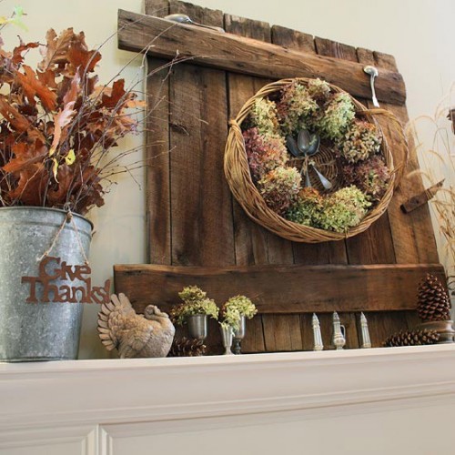 a Thanksgiving mantel with a wooden board, a basket with hydrangeas and spoons, pinecones, fall leaves and a turkey figurine
