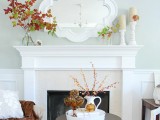 neutral candles in candleholders and bright fall leaves on branches for decorating your mantel for Thanksgiving in modern style