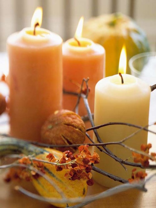 a modern rustic centerpiece of branches, blooms, pumpkins and natural-colored candles for fall and Thanksgiving