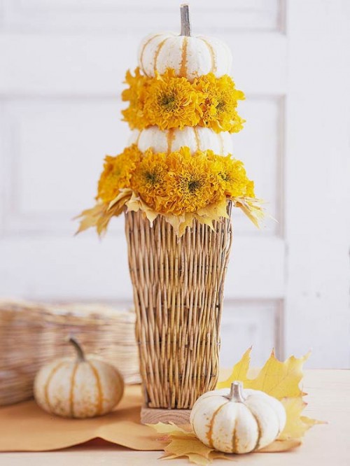 a tall basket with bright blooms and pumpkins, wiht leaves and pumpkins around is a cool fall centerpiece