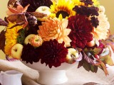 a bold and bright Thanksgiving centerpiece of a bowl with fruits and bright blooms and fall leaves is very cool