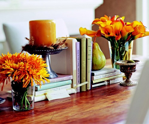 a simple Thanksgiving centerpiece of bright blooms in glass vases and a rust-colored candle in a candleholder