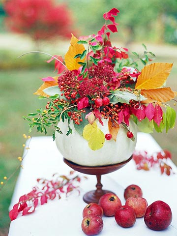 a wood stand with a pale pumpkin, bright leaves, berries and bold blooms is a lovely and chic fall centerpiece to rock
